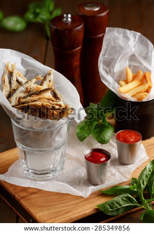 Close-up of beer snacks, sprat and french fries with gravy on wooden table