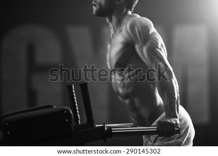 Young strong man black and white portrait. Muscular bodybuilder doing exercise on bars in the gym