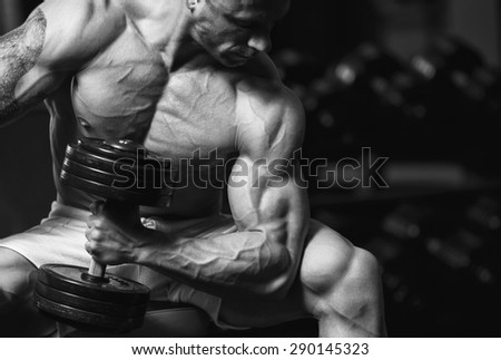 Young strong man black and white portrait. Strong muscular bodybuilder doing exercise with dumbbell in the gym