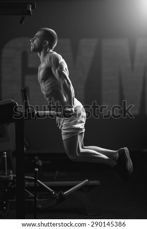 Young strong man black and white portrait. Muscular bodybuilder doing exercise on bars in the gym