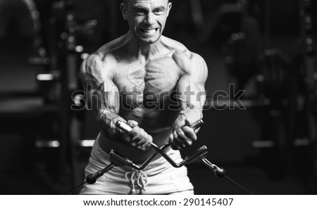 Young strong man black and white portrait. Muscular bodybuilder doing exercise on the chest in the crossover in the gym
