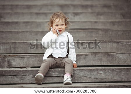 Cute little girl in white knitted sweater talking on mobile phone outdoors