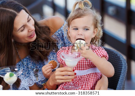 Happy mom and daughter eating ice cream and drinking coffee outdoors. Family sitting at a table in the outdoor cafe and eating ice cream.