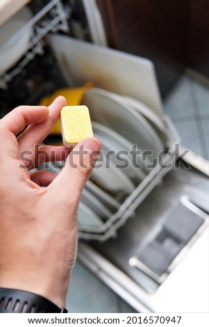 the man puts a tablet in the dishwasher. washing dishes in a dishwasher
