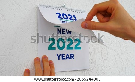 Close-up of male hands flipping through the December page of 2021 wall calendar followed by the title page of a new 2022 calendar