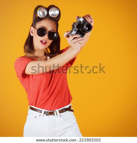 Young attractive fashionable surprised woman with old-school camera wearing glasses