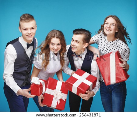 Group of smiling young people holding presents wrapped in red gift paper. Hipster style. Blue background. Standing together happy smile give wrapped giftboxes