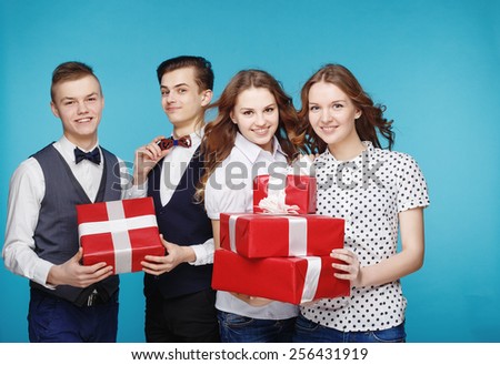 Group of smiling young people holding presents wrapped in red gift paper. Hipster style. Blue background. Standing together happy smile give wrapped giftboxes