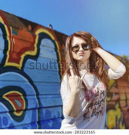Portrait of Trendy Hipster Girl Standing at the Graffiti Brick Wall Background. Urban Fashion Concept. Copy Space.