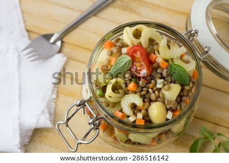 Jar with salad of vegetables, pasta and lentils on a wooden surface