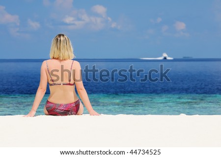 Young woman sitting at the beach against sea and speed boat at horizon