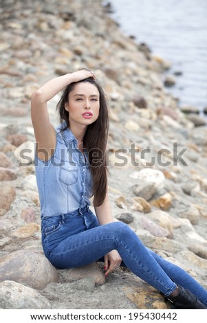 Sad woman sitting on rocks on the river arms folded on her lap and staring into the distance