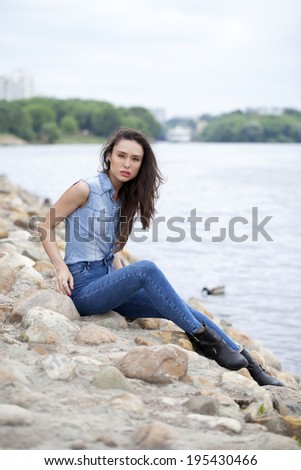 Sad woman sitting on rocks on the river arms folded on her lap and staring into the distance