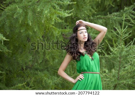 Beautiful young woman in green dress, against green of summer park