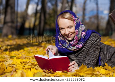 Portrait of young woman lying on autumn leaves with book in autumn park