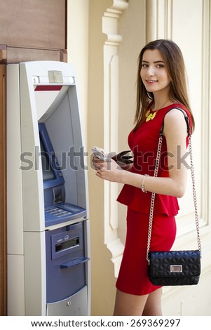 Brunette young lady using an automated teller machine . Woman withdrawing money or checking account balance