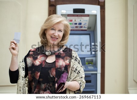 Mature blonde woman with credit card in hand near automated teller machine in shop