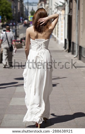 Full length portrait of beautiful model woman walking in white dress in summer street