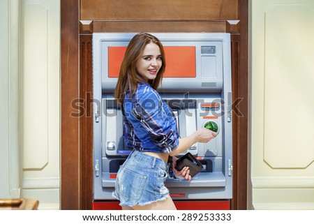 Brunette young lady using an automated teller machine . Woman withdrawing money or checking account balance