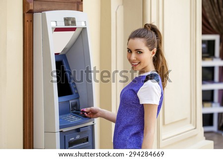Brunette young lady using an automated teller machine. Woman withdrawing money or checking account balance