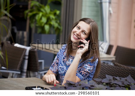 Young beautiful woman sitting in a summer cafe and talking on cell phone