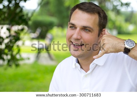 Attractive 30 years old caucasion man making a call me gesture, outdoors summer park
