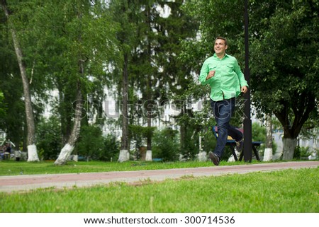 Happy young man in a green shirt and blue jeans running on summer park