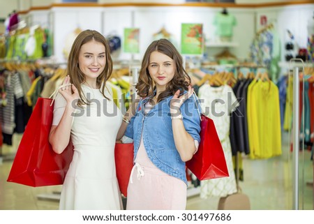 Two young beautiful girls standing at the storefront with shopping bags