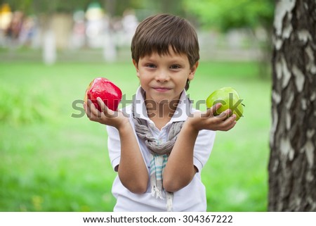 Closeup portrait of beautiful little boy holds two apples on the background of summer park