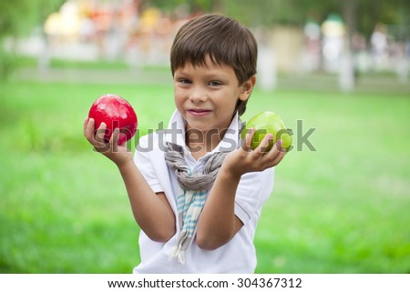 Closeup portrait of beautiful little boy holds two apples on the background of summer park