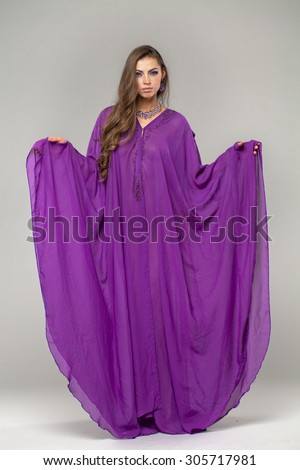 Beautiful young woman in purple tunic Arabic, on gray background