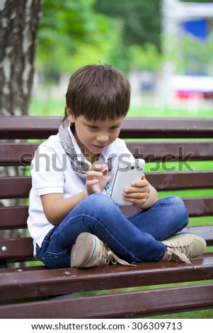 Little boy intently playing games on smartphone on a background of summer park