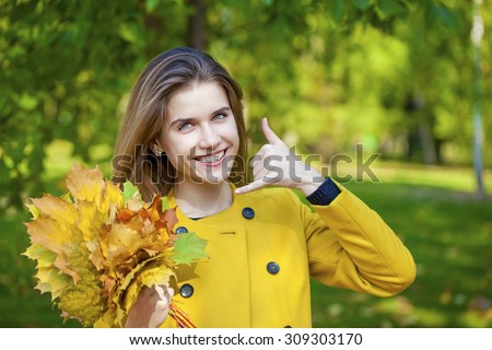 Beautiful woman making a call me gesture in autumn park