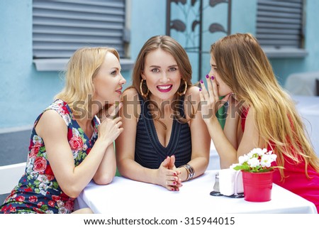Three beautiful girlfriends gossiping woman sitting in the summer city cafe