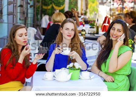 Three young beautiful girls girlfriend drinking tea in a summer cafe