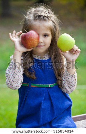Portrait of a little girl with two large apples on a background of autumn park