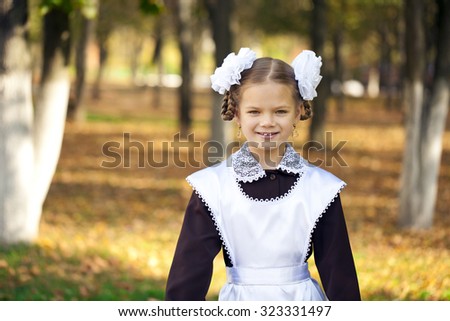 Portrait of a beautiful young first-grader in a festive school uniform on the background autumn park