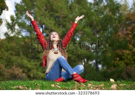 Young beautiful woman in red leather jacket and blue jeans sitting in the autumn park