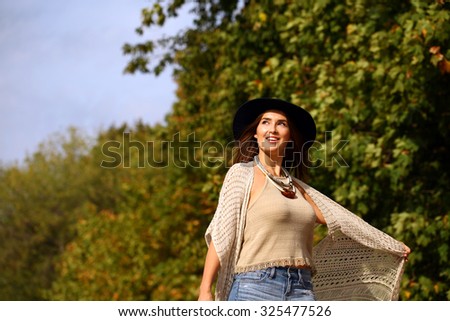 Young beautiful woman in fashion blue ripped jeans and red bag walking in autumn park