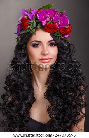 beautiful girl with a wreath of orchids and roses on head. Glamorous woman in black leather corset. long black curly hair.Beauty woman with perfect fashion makeup.