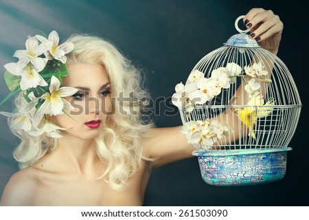 beauty portrait of a girl with a lily in her hair. Blonde holding a cage with a bird on a gray background.woman holding vintage bird cage