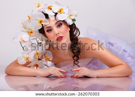 Beautiful sexy brunette woman with  orchids flower in her hair and her reflection in mirror table  with perfect skin