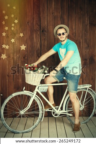 Young man riding a bike.hippie hat and glasses on old bicycle on a background of a wooden wall