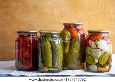 Glass jars with pickled cucumbers (pickles), pickled tomatoes and cabbage. Jars of various pickled vegetables. Canned food in a rustic composition.