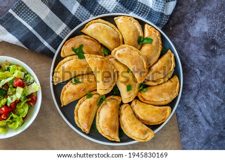 Empanadas - traditional Latin American baked beef pastry on a plate with a fresh salad side dish. Gluten free savory pastries with meat stuffing or filling. Handmade typical dish in Spain or Argentina