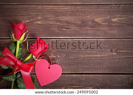 Valentine background of gift tag and two red roses with ribbon and bow on wood. Space for copy.