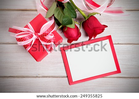 Valentine background of gift box, two red roses and blank card with envelope on wood. Space for copy.