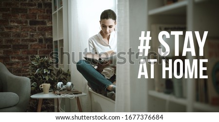 Young woman isolating at home and relaxing, she is reading a book: stay at home social media campaign for coronavirus prevention