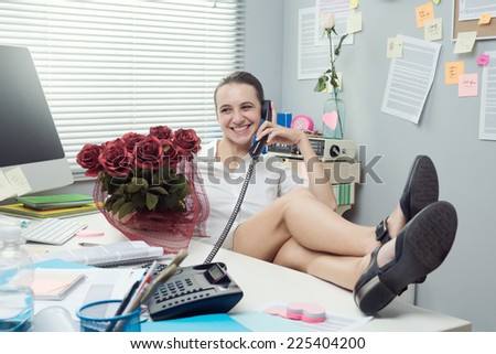 Female office worker feet up on desk talking on the phone and holding roses.