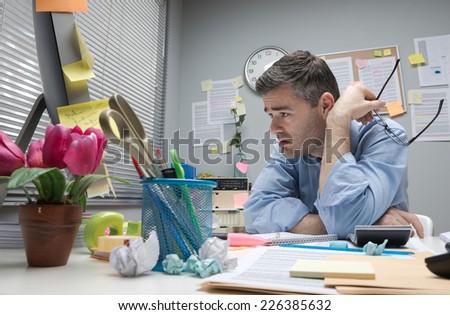 Depressed bored office worker at his desk holding glasses.